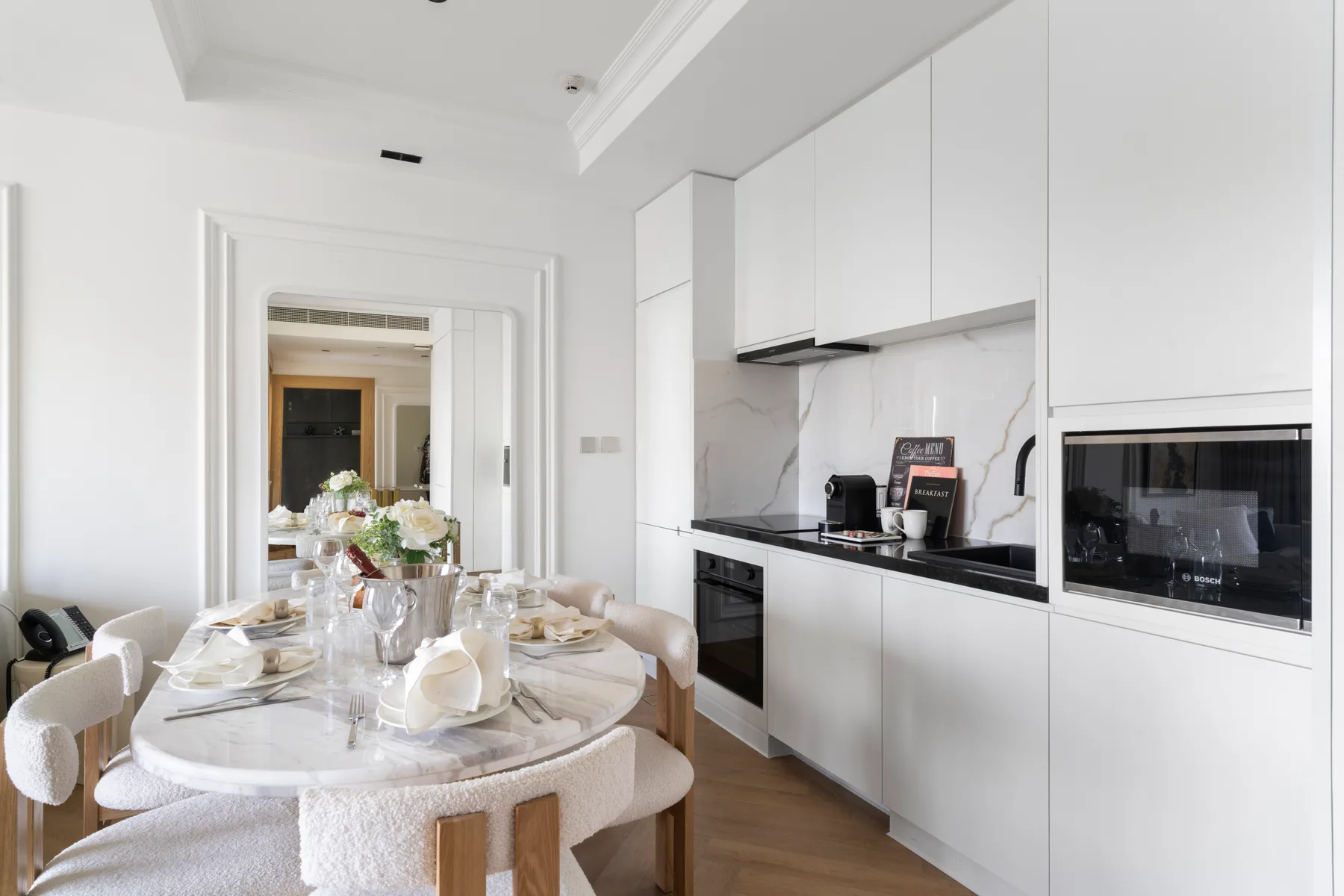 Un comedor luminoso junto a una cocina moderna, con la mesa preparada para comer.