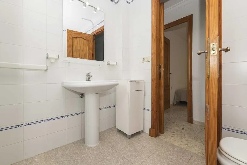 A tiled bathroom with a pedestal sink, mirror, and wooden doorway.