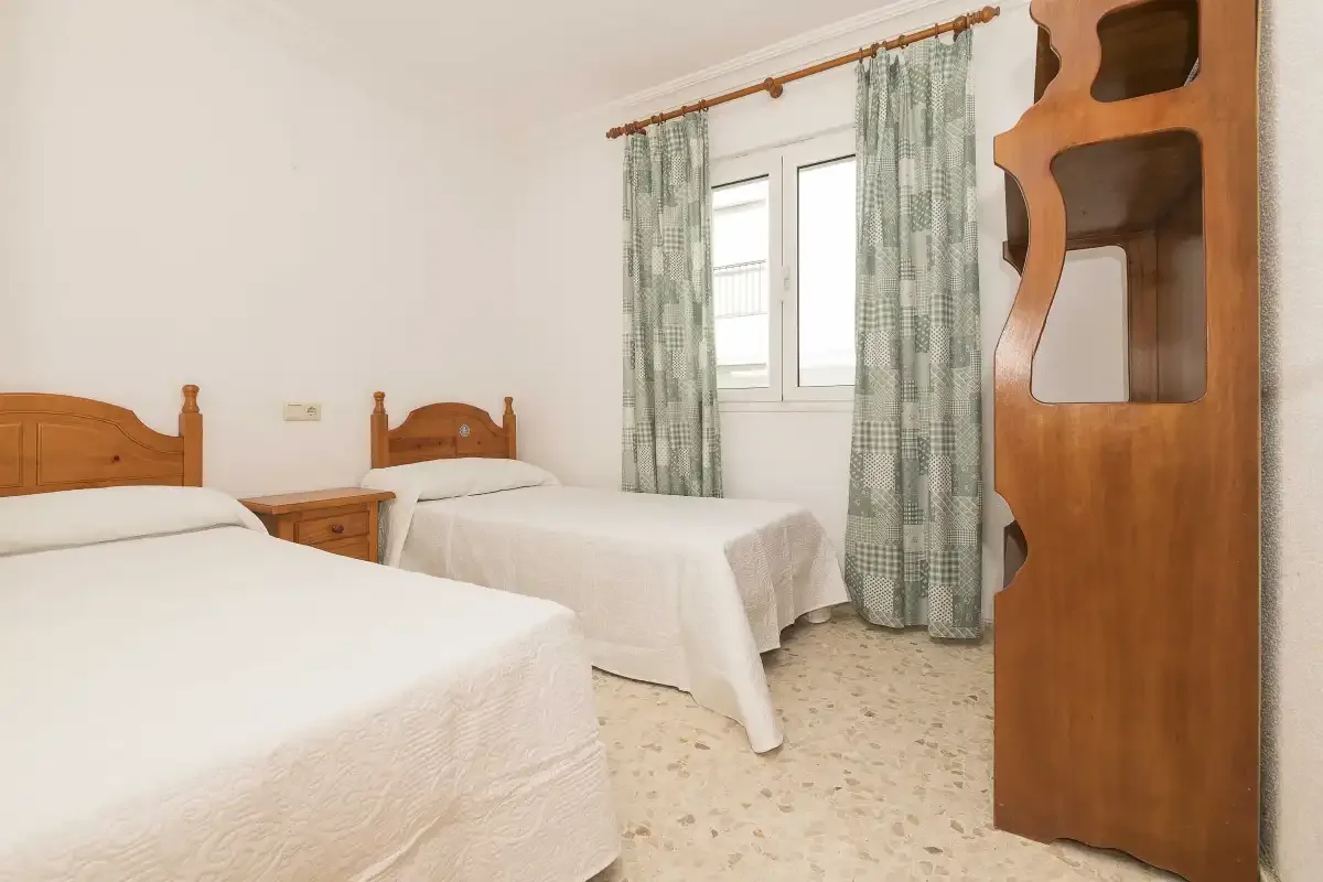 A bedroom with two beds and a window with green curtains.