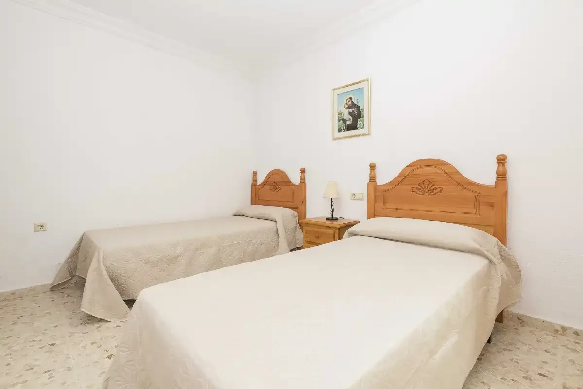 A bedroom with two beds, a bedside table, and a framed picture.