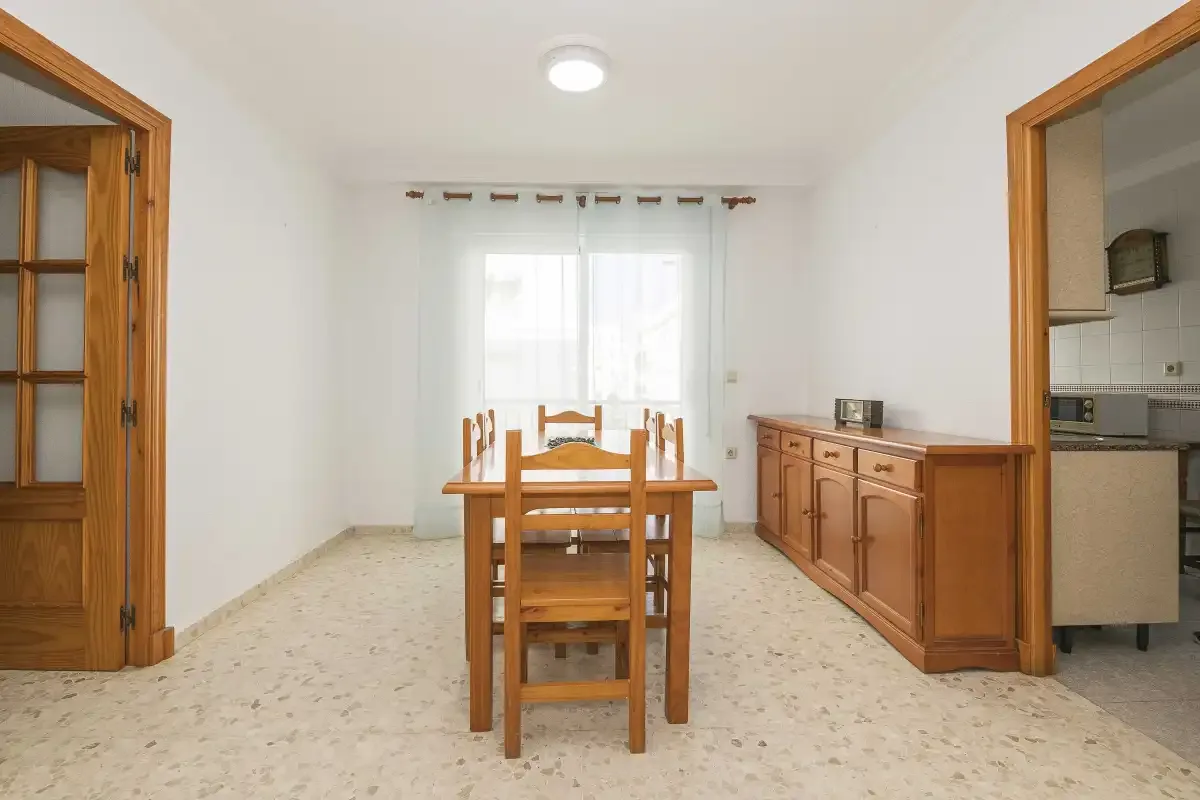 A dining area with a wooden table and chairs beside a kitchen counter.