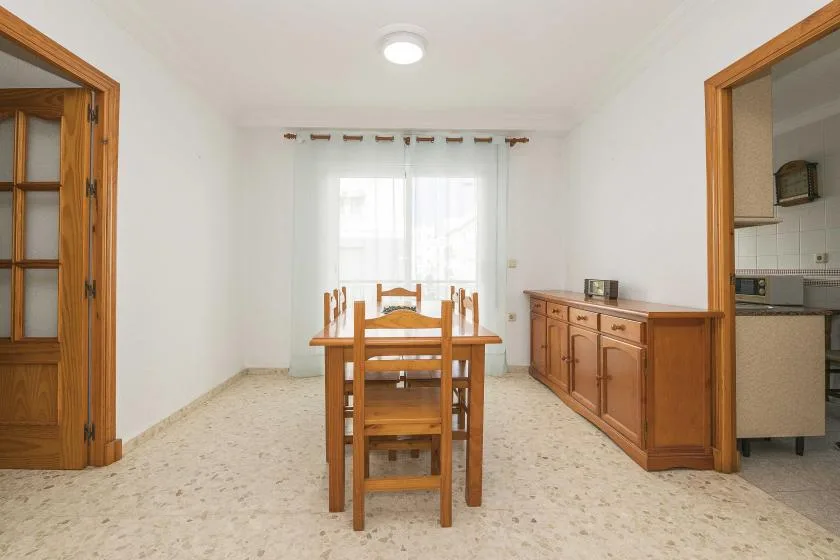 A dining area with a wooden table and chairs beside a curtained window.