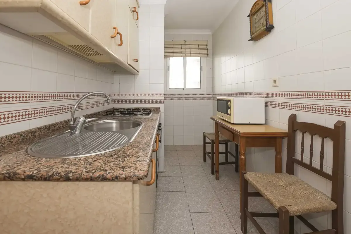 A narrow kitchen with a sink, counter, and small dining table.