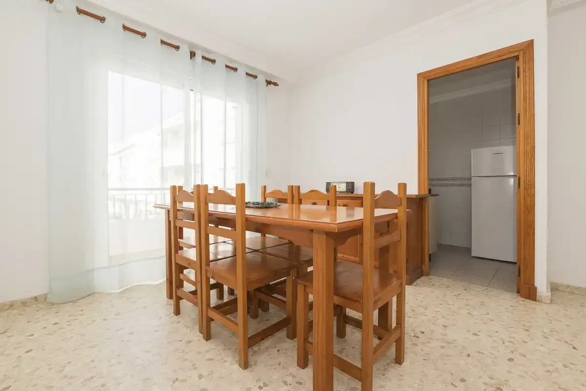 A dining area with a wooden table and seating beside a curtained window.