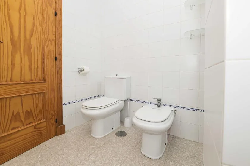 A tiled bathroom with a toilet and bidet beside a wooden door.