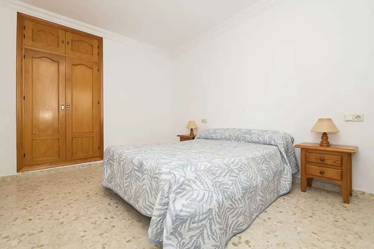 A bedroom with a double bed covered in a pale patterned bedspread.