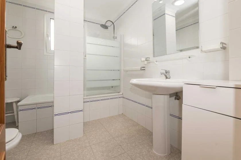 A bright tiled bathroom with a glass shower, pedestal sink, and mirrored cabinet.