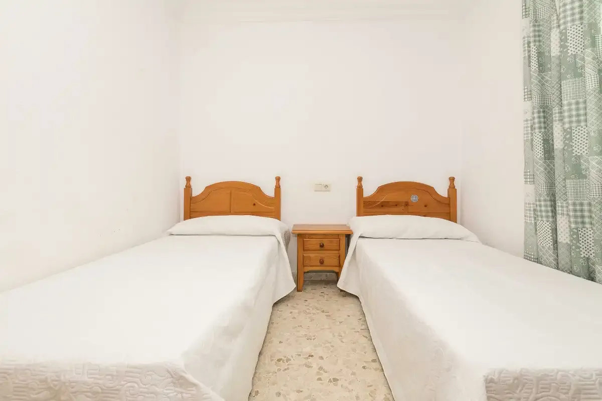 A twin bedroom with two single beds and a wooden bedside table.