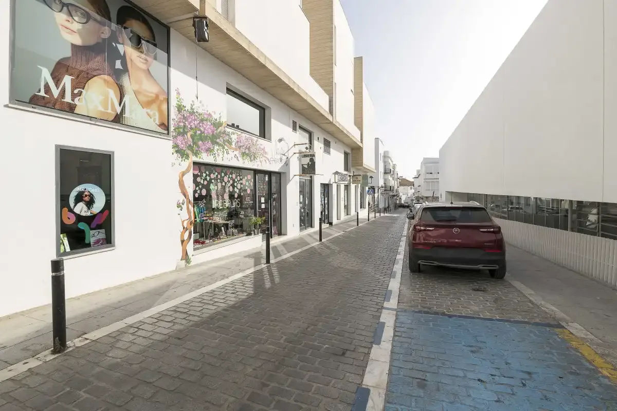 A paved street runs between storefronts and a parked car.