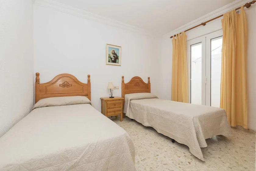 A bedroom with two beds, a bedside table, and curtained glass doors.