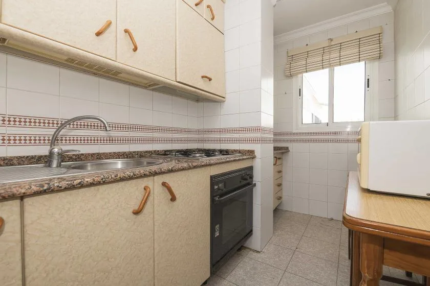 A tiled kitchen with a countertop, sink, and window.