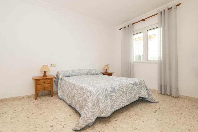 A bright bedroom with a bed beside a curtained window.