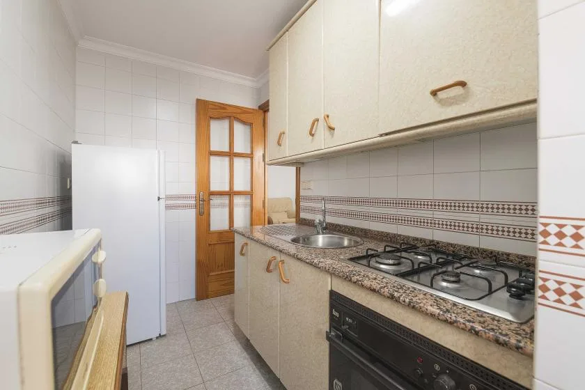 A tiled kitchen with countertop cabinets, a refrigerator, and a gas cooktop.