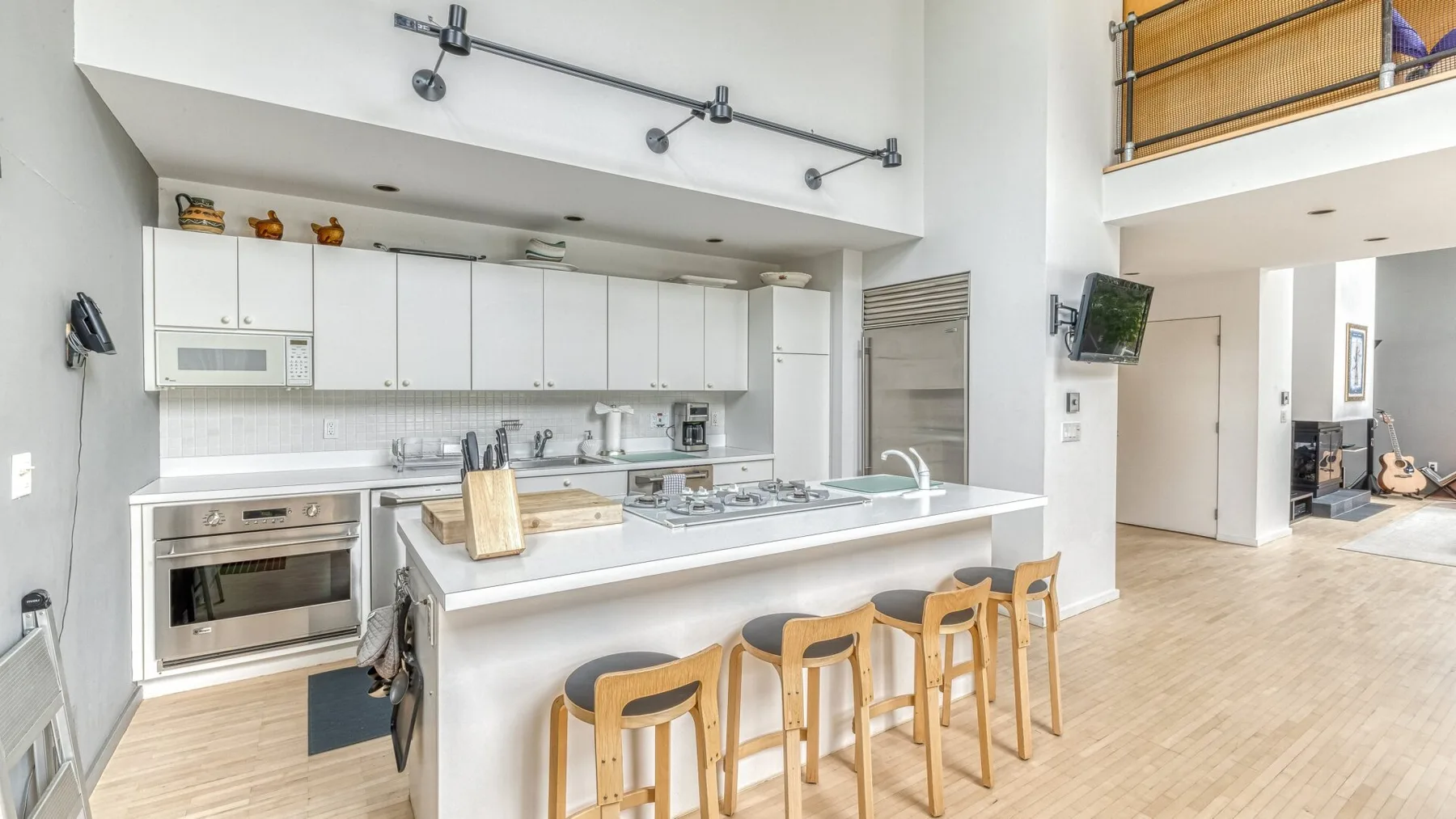A bright kitchen with white cabinets, a central island, and wooden stools.