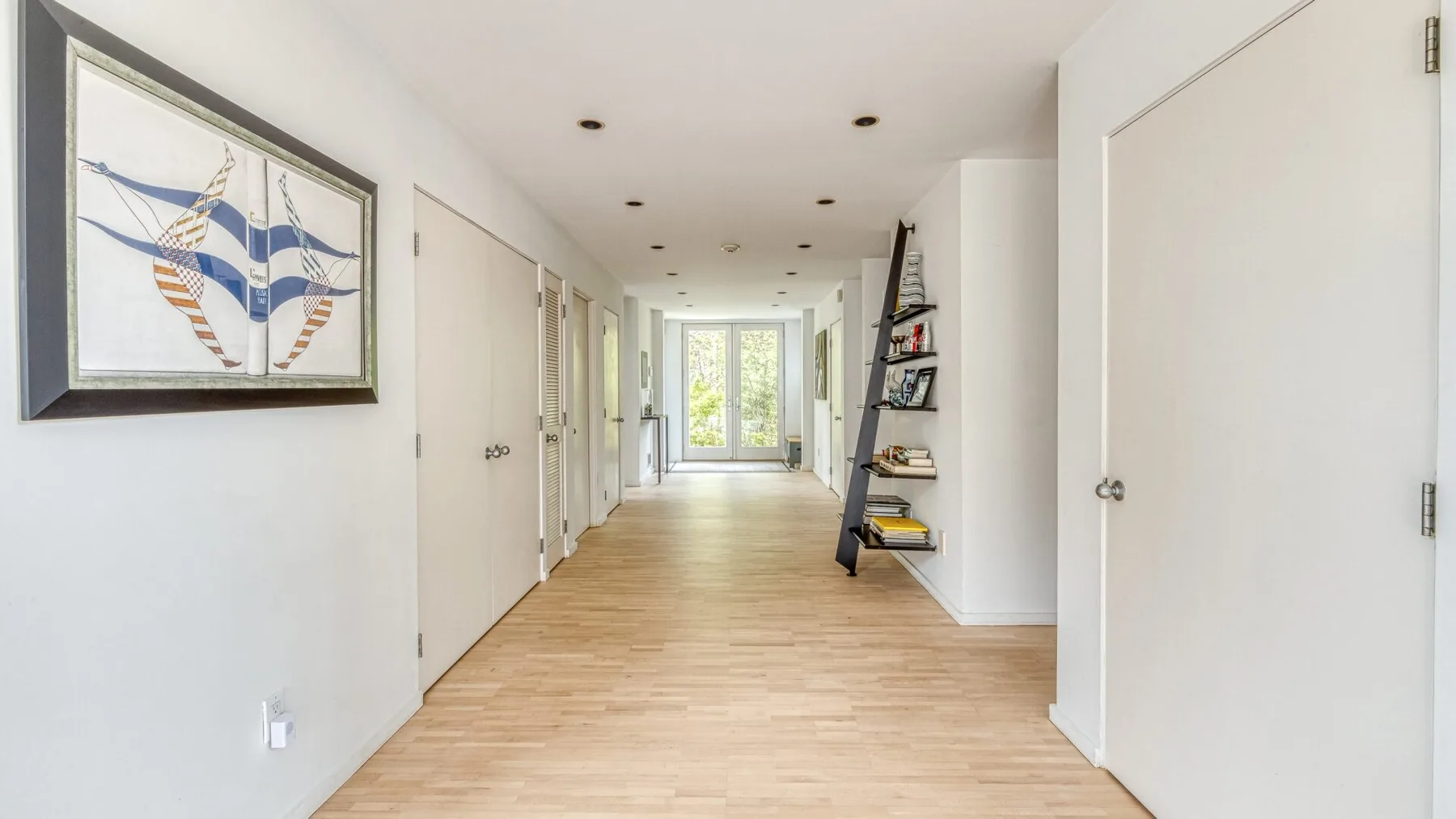 A bright hallway with light wood flooring and framed artwork on the wall.