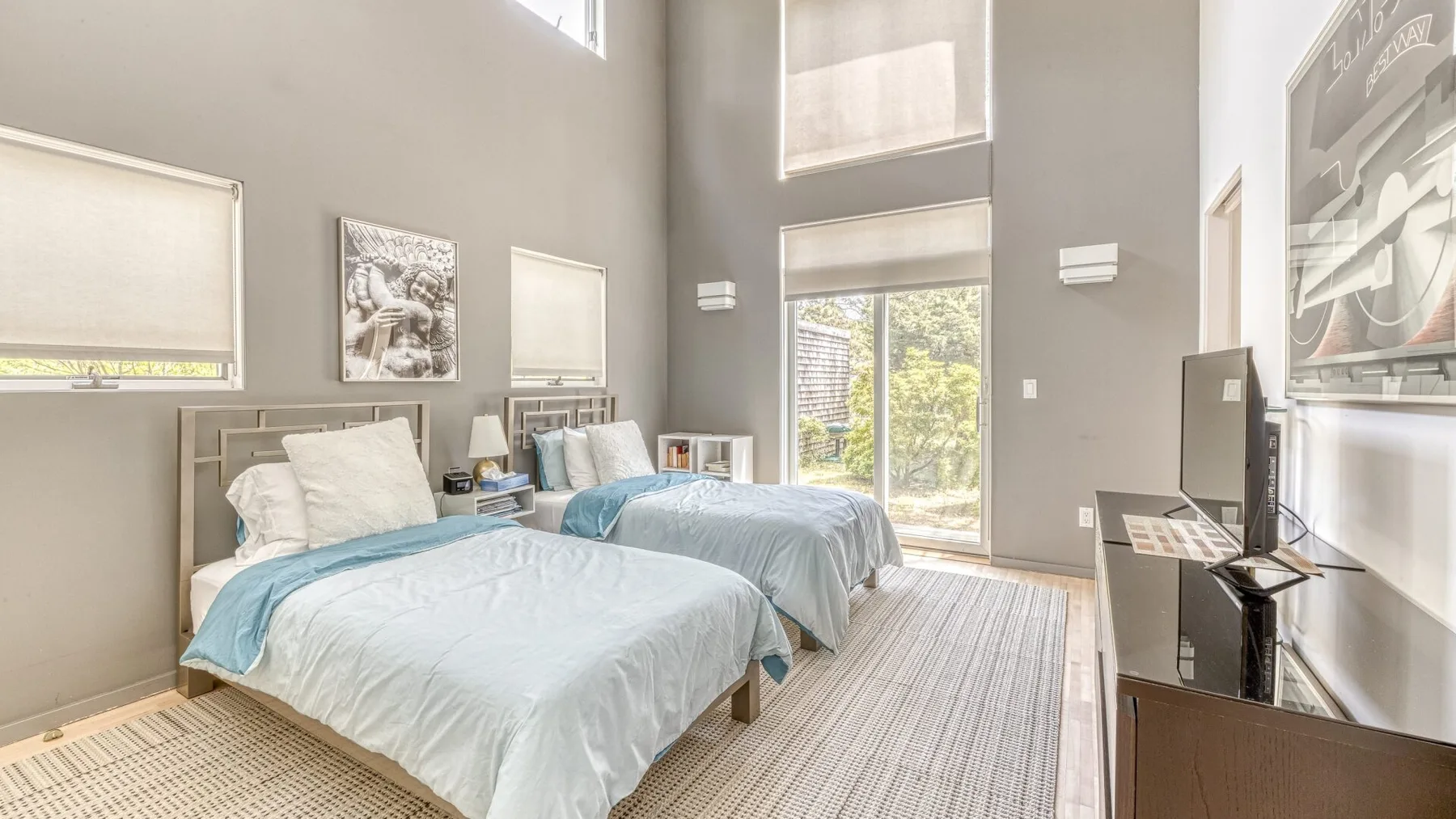 A bright bedroom with two beds, light bedding, and a large window.