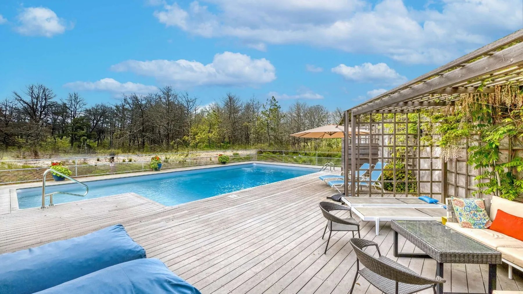 An outdoor swimming pool beside a wooden deck and shaded seating area.