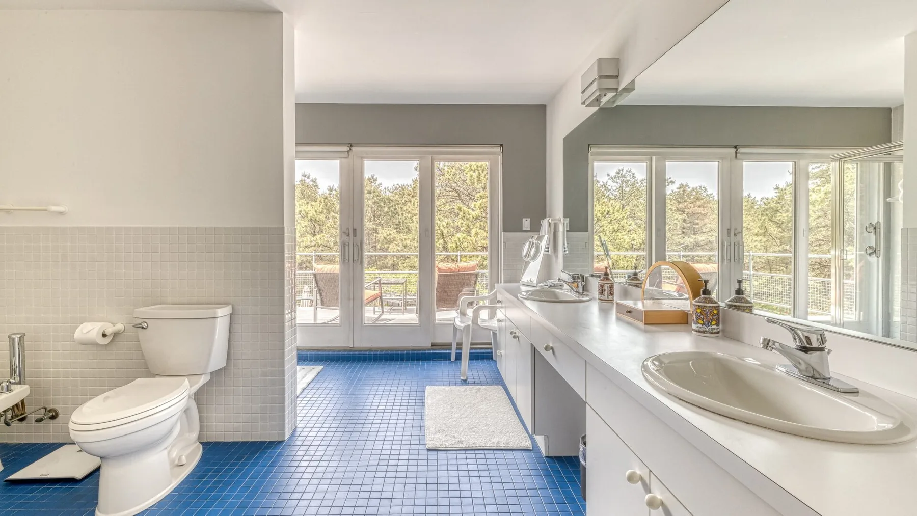 A bathroom with a toilet, vanity, and large windows overlooking trees.