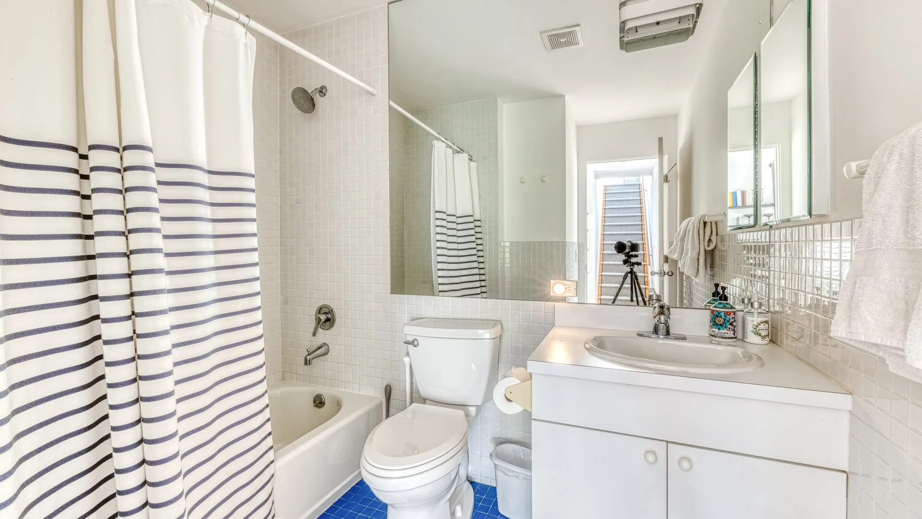 A bright bathroom has a bathtub with a striped shower curtain beside a sink.