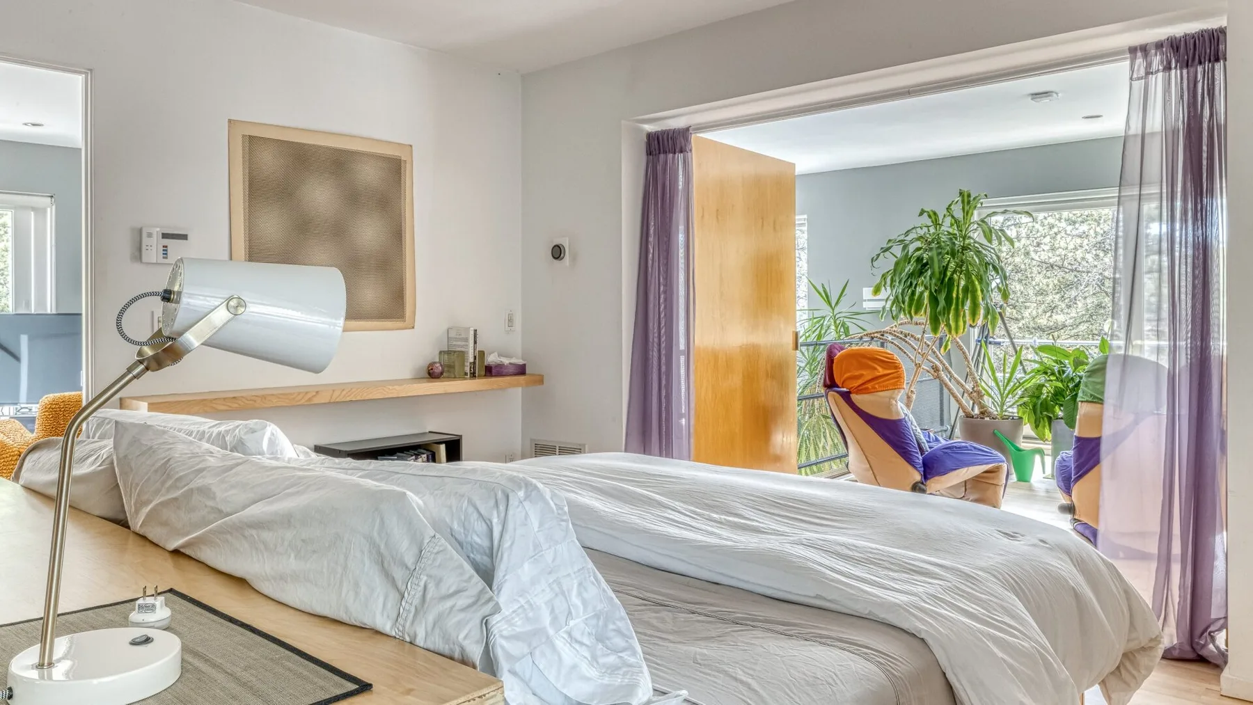 A bedroom with an unmade bed and a sitting area beside a bright window.