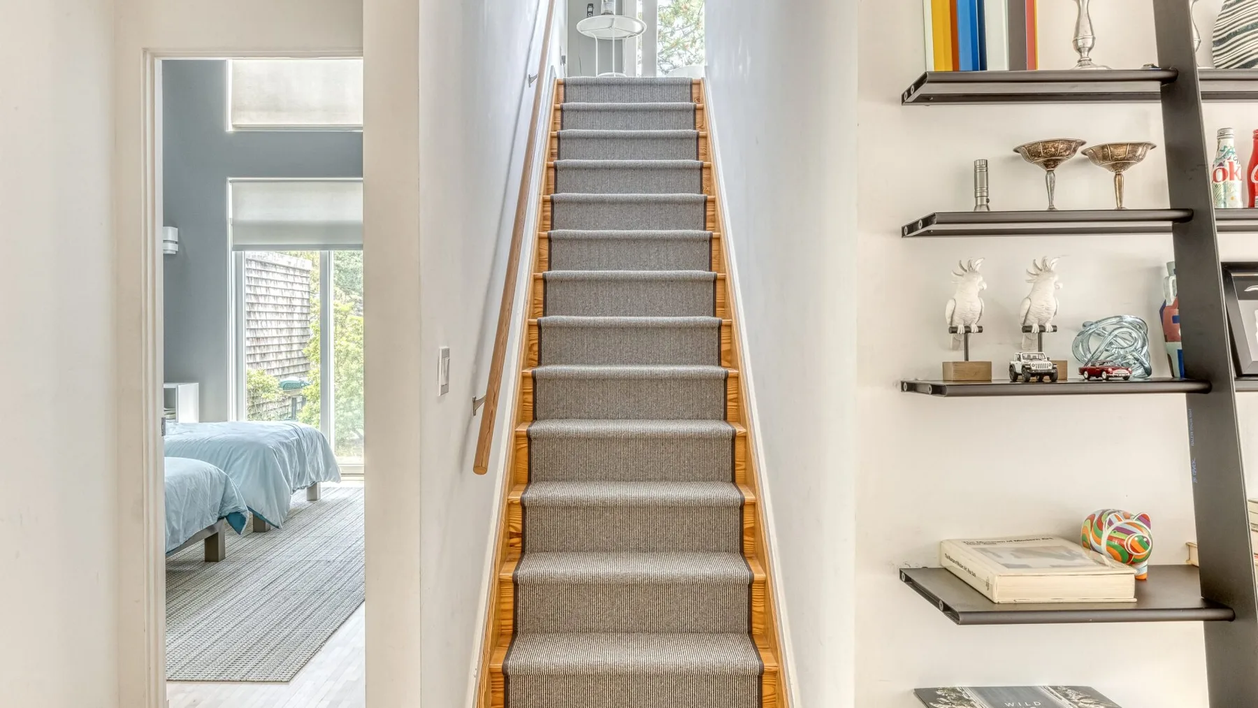 A carpeted staircase with wooden handrails stands beside wall-mounted display shelves.