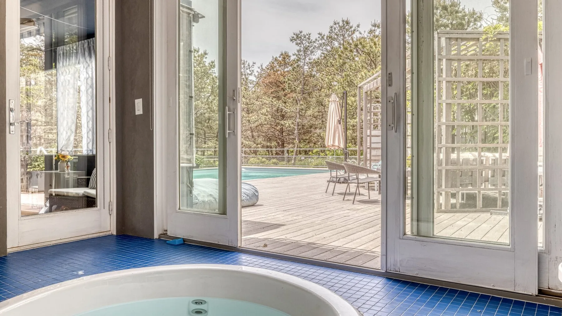 A sunlit room opens onto a deck with a pool and outdoor seating.
