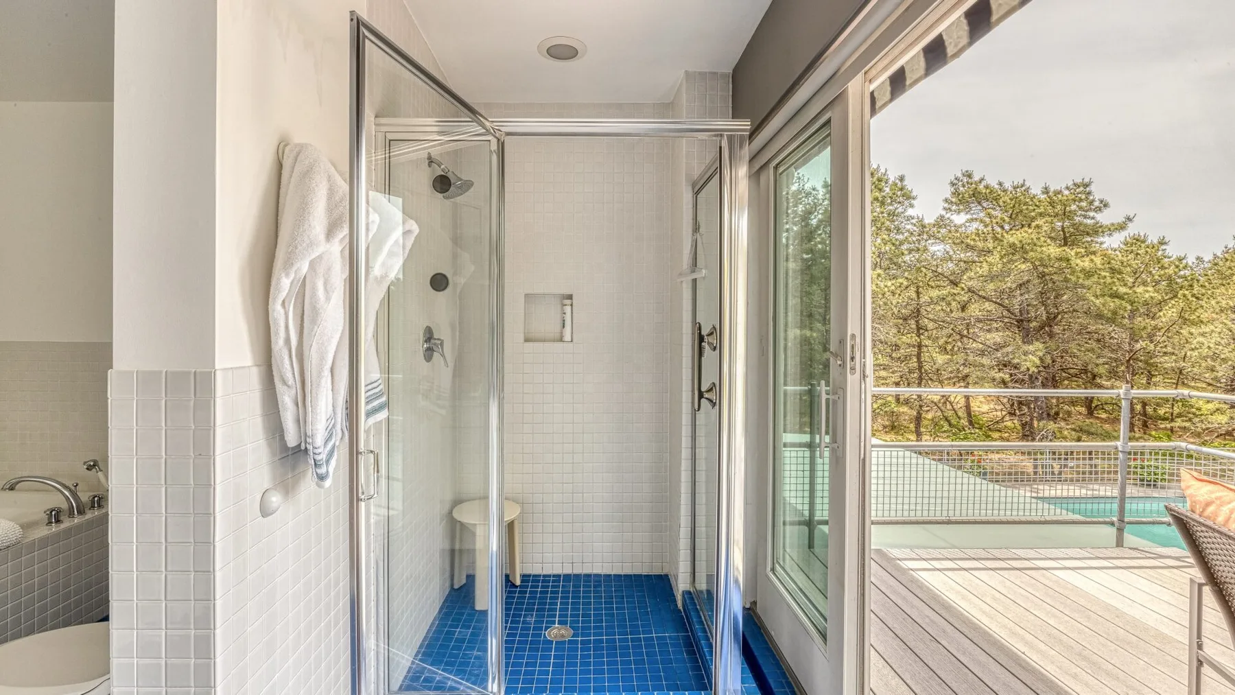 A bathroom with a glass shower beside a large window overlooking a deck.