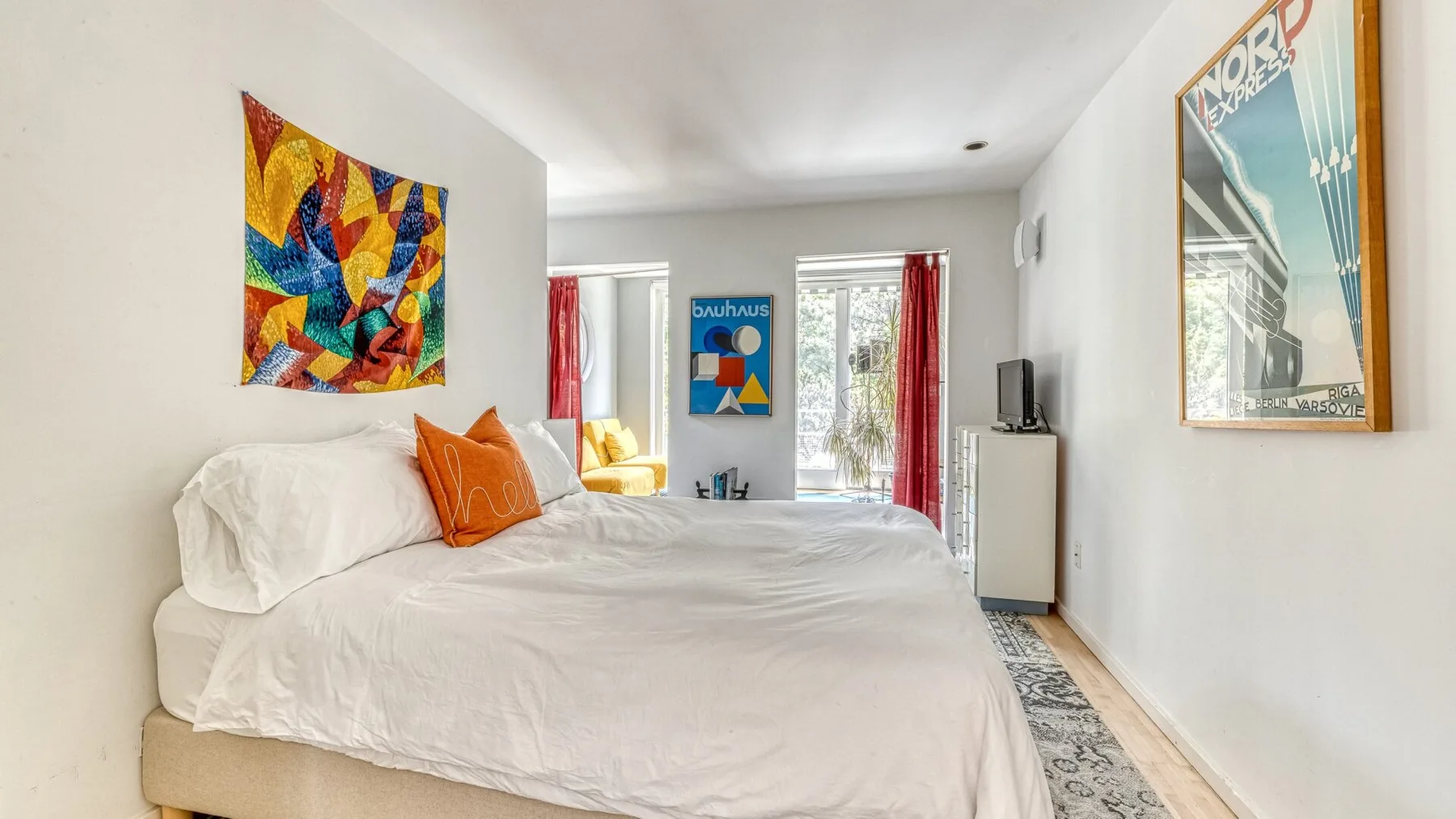 A bright bedroom with a neatly made bed and colorful wall art.
