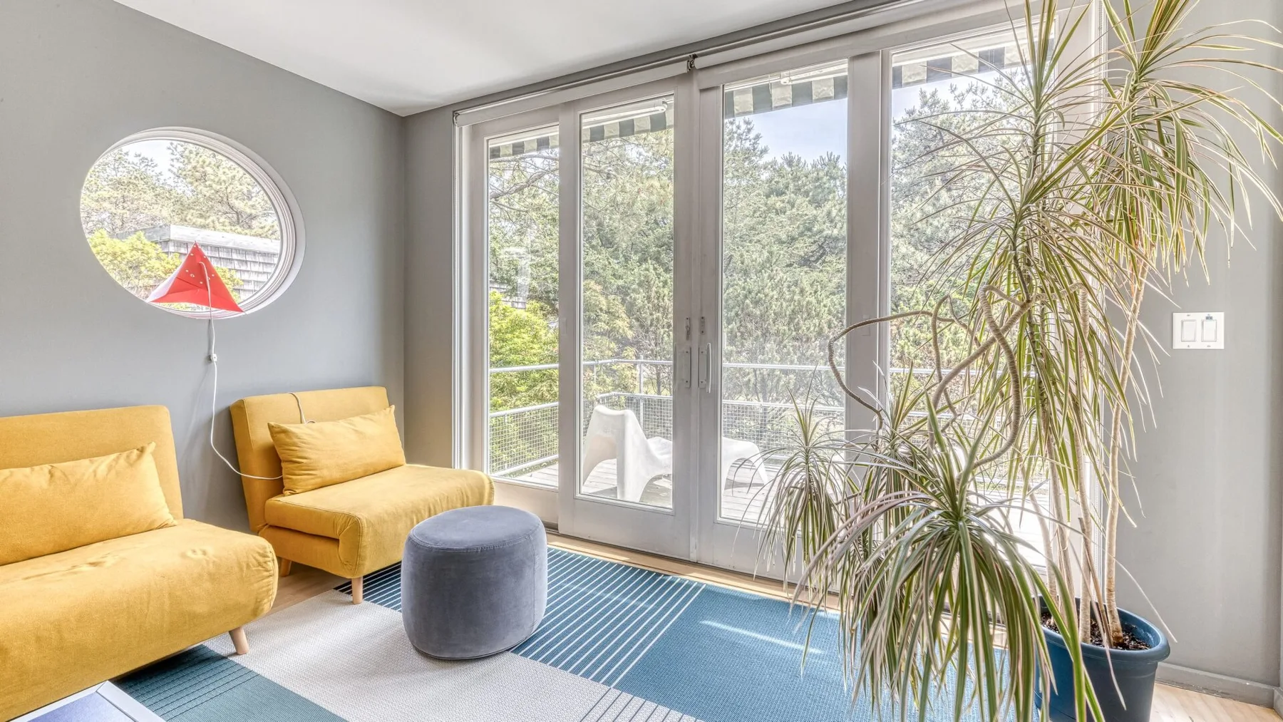 A bright sitting area with yellow seating, a round ottoman, and large glass doors.