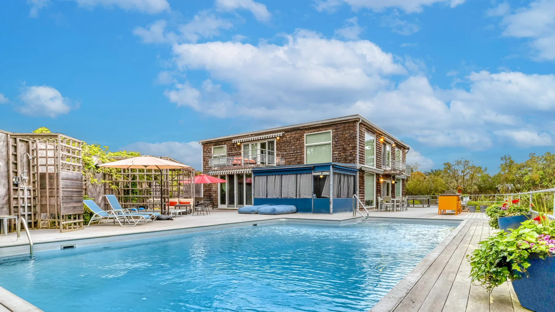 An outdoor swimming pool sits beside a modern building and landscaped patio.