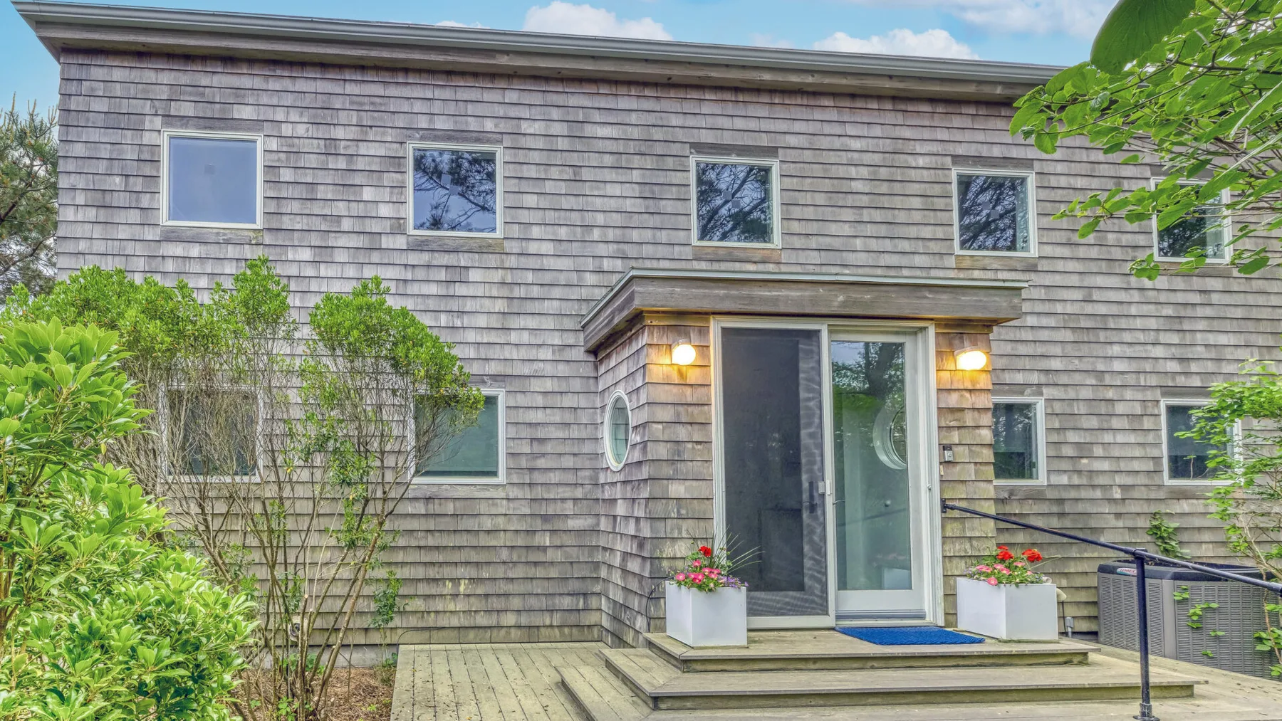 A shingled house exterior with a glass entry door and surrounding greenery.