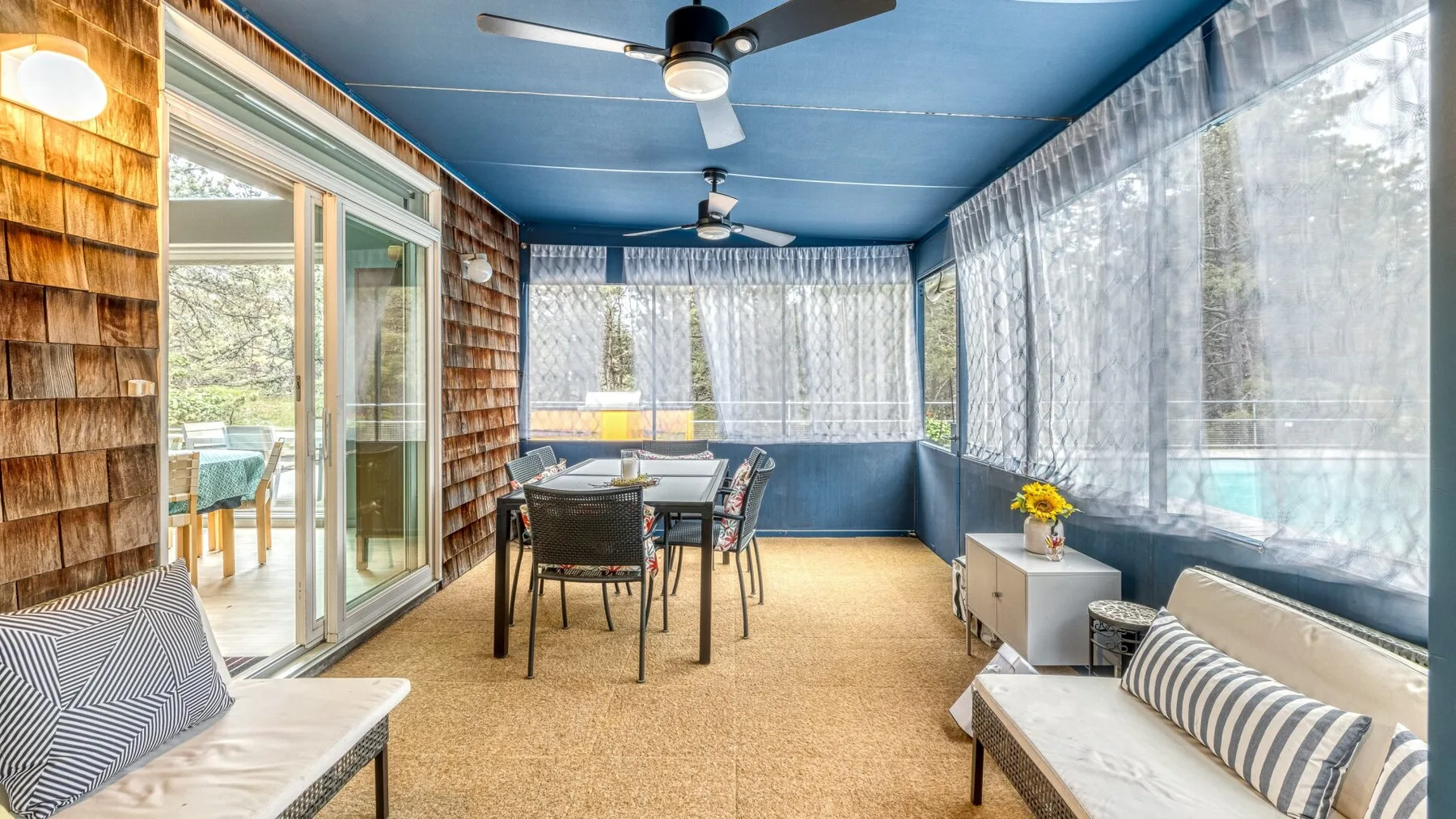 A bright enclosed patio with a dining table, seating, and large windows.