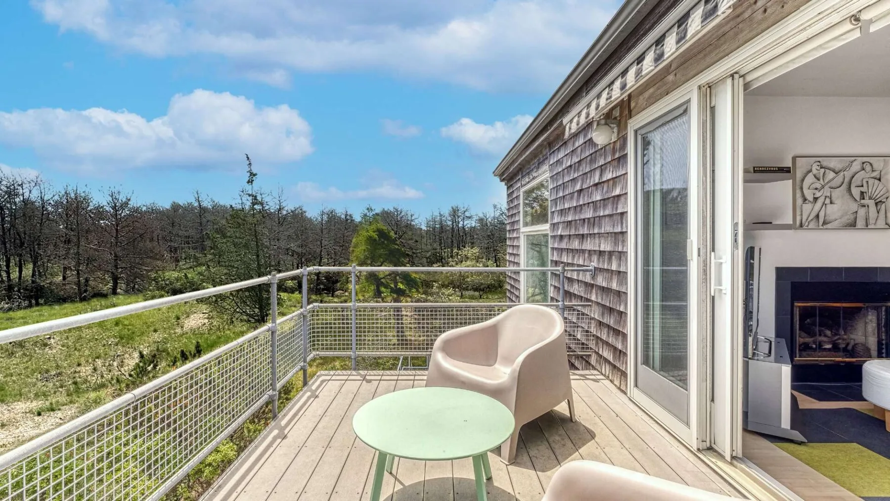 A wooden deck overlooks a grassy landscape, with outdoor seating beside sliding glass doors.