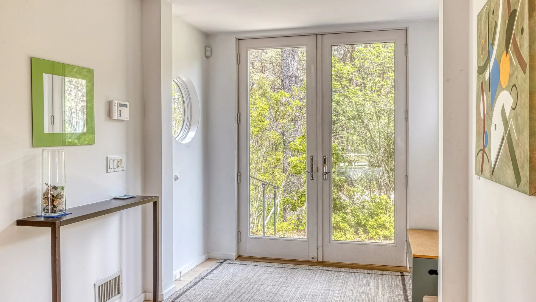 A bright room opens onto a leafy outdoor view through glass doors.