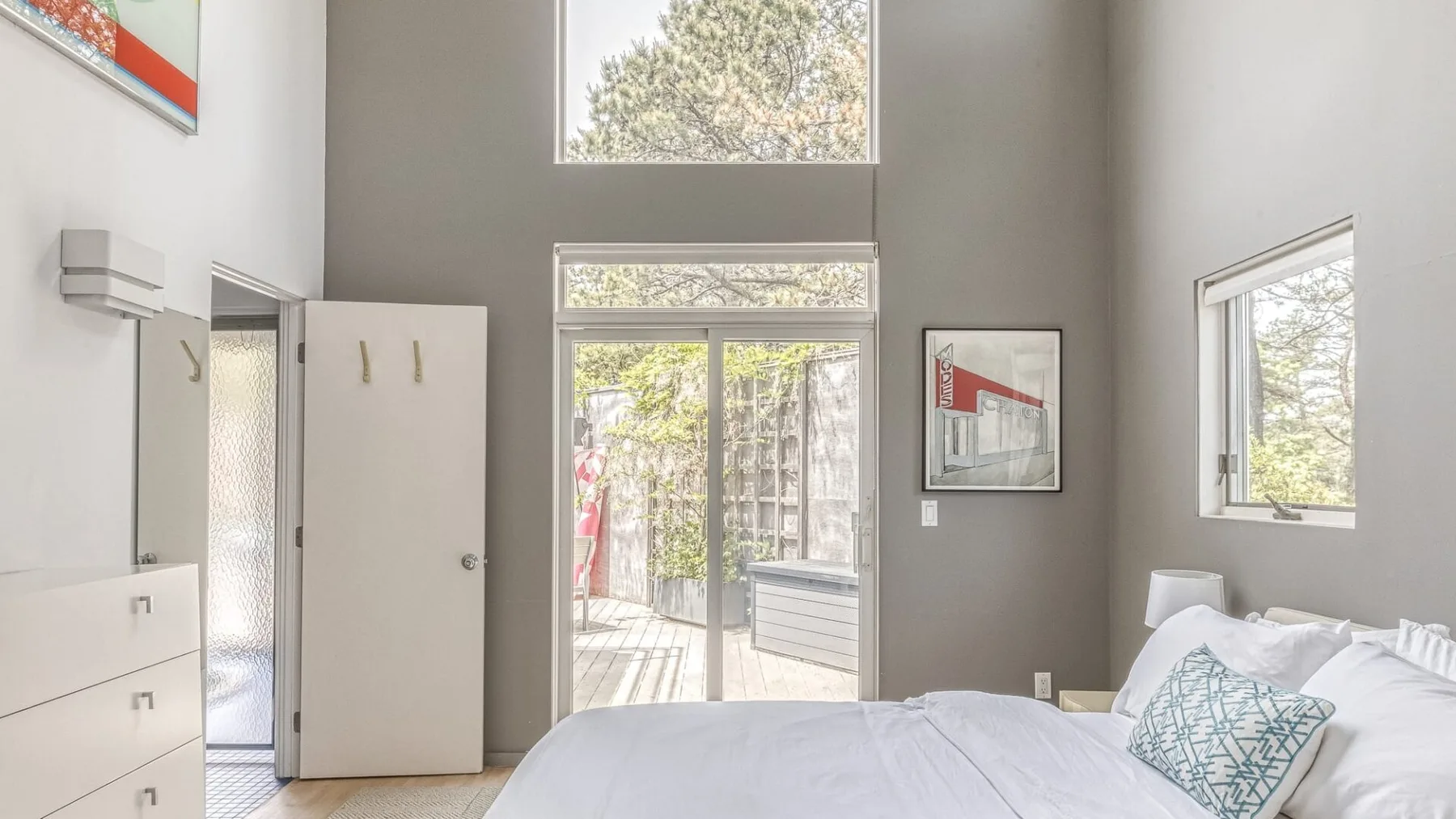 A bedroom with a bed beside tall windows and a glass patio door.