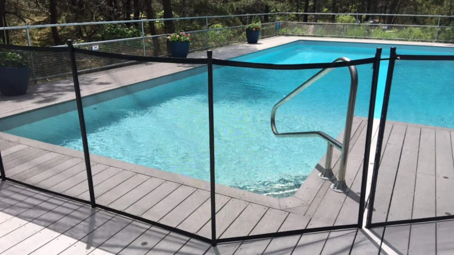 An outdoor swimming pool is surrounded by a wooden deck and safety fence.