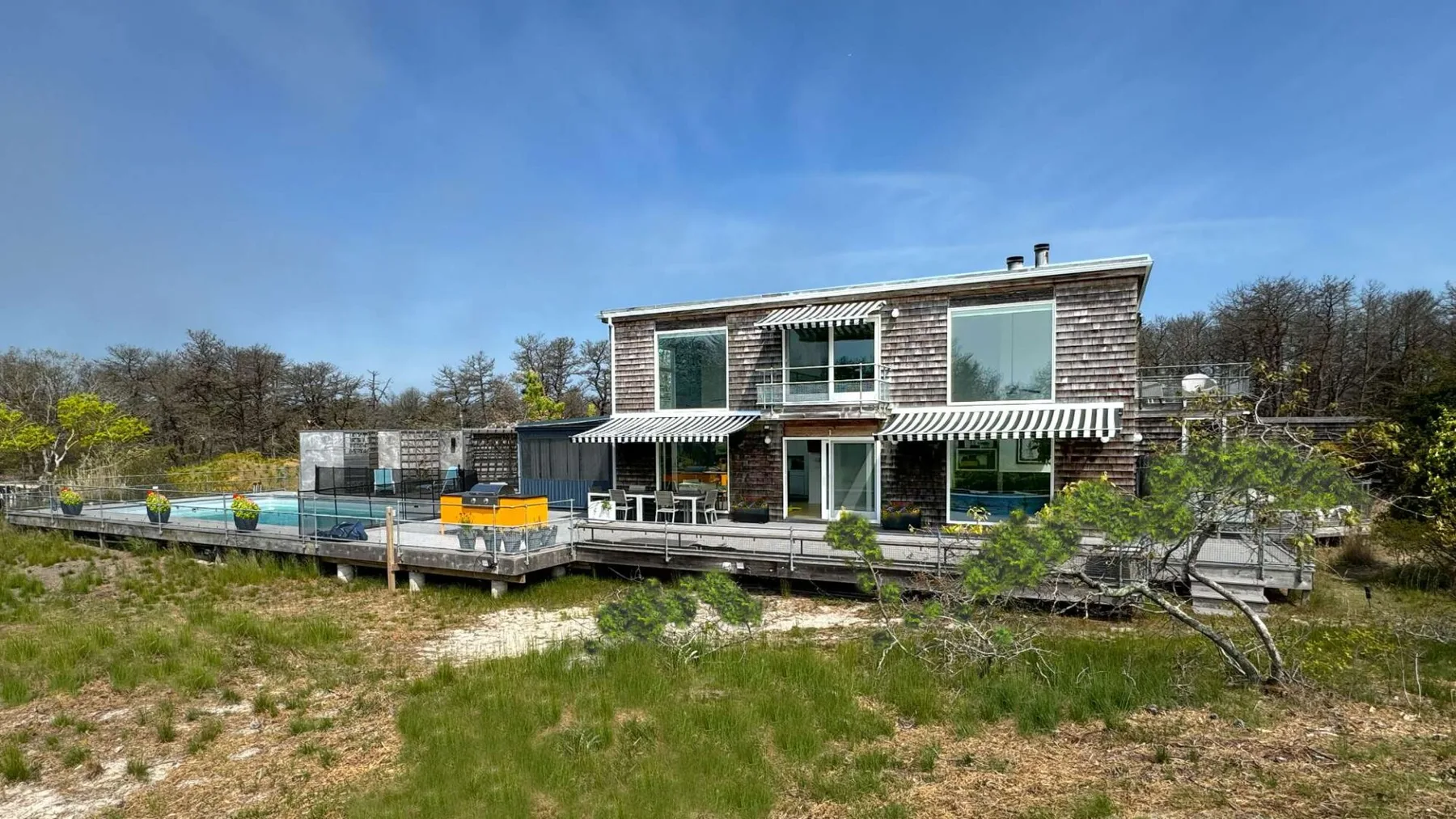 A modern house stands beside a wooden deck and swimming pool.