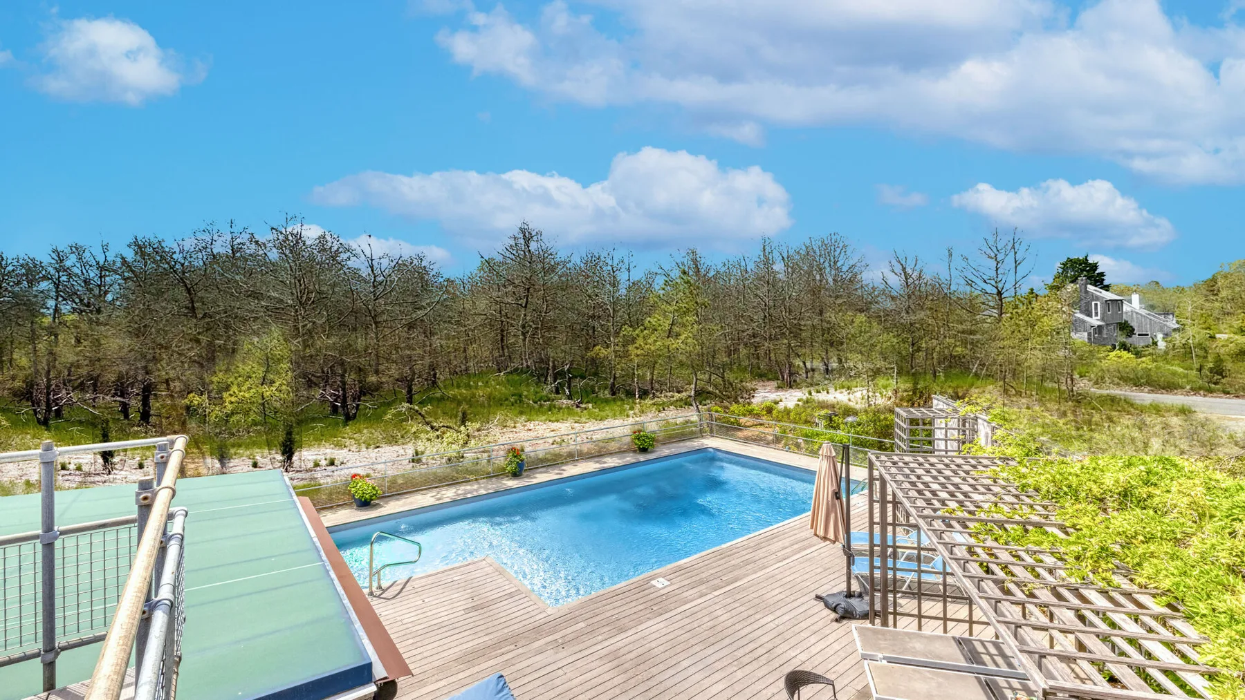 An outdoor swimming pool beside a wooden deck, with trees in the background.