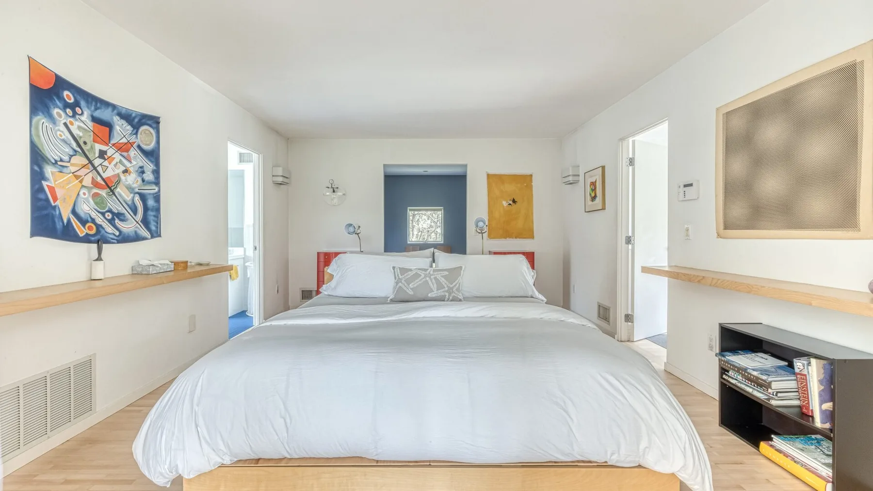 A bright bedroom with a neatly made bed and colorful wall art.