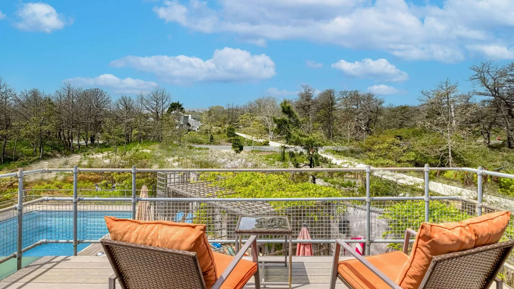 An outdoor poolside deck with orange-cushioned seating and a view of green grounds.