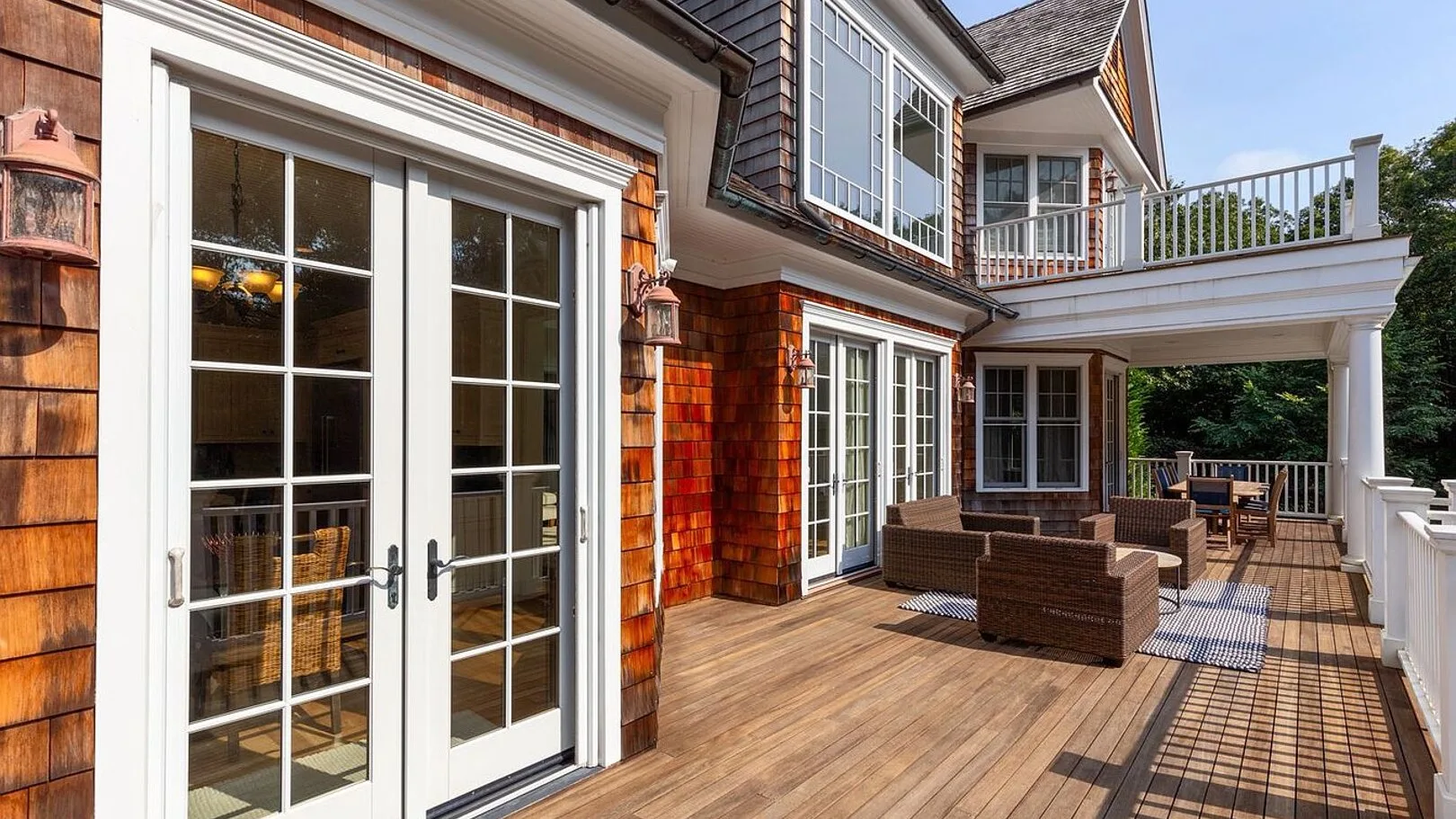A wooden deck with outdoor seating extends along the house beside glass doors.