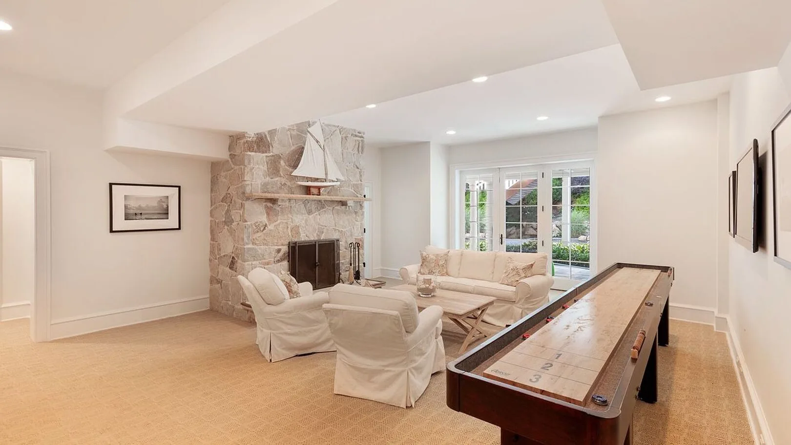 A bright living room with seating, a stone fireplace, and a shuffleboard table.