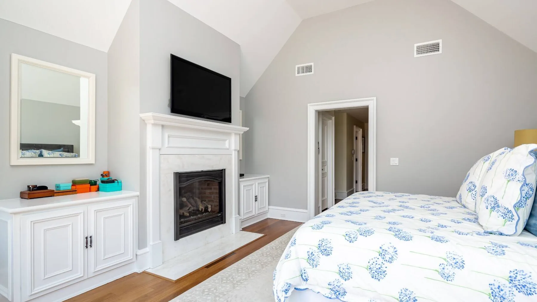 A bedroom with a fireplace, television, and bed covered in blue floral bedding.