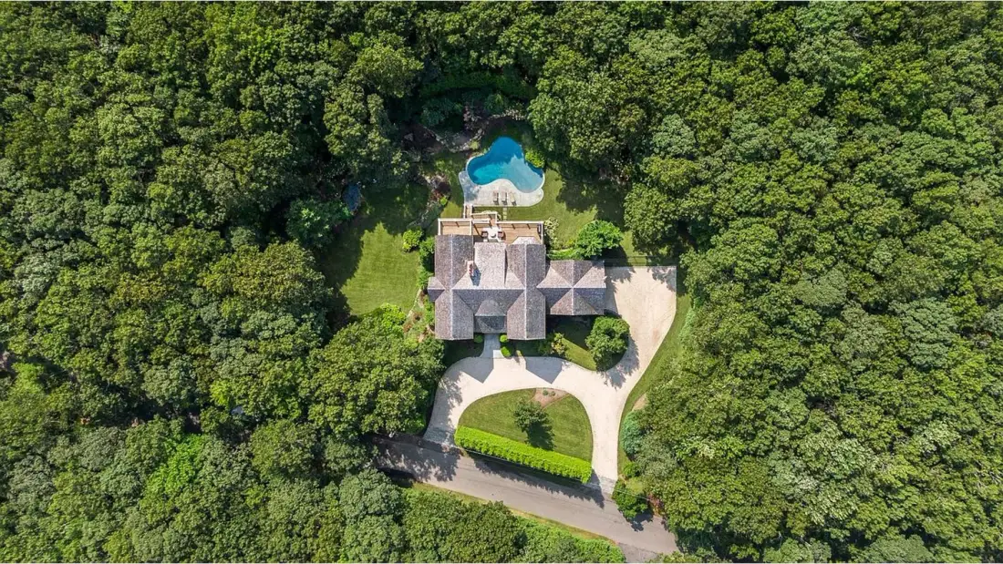 Aerial view of a house and swimming pool surrounded by dense trees.