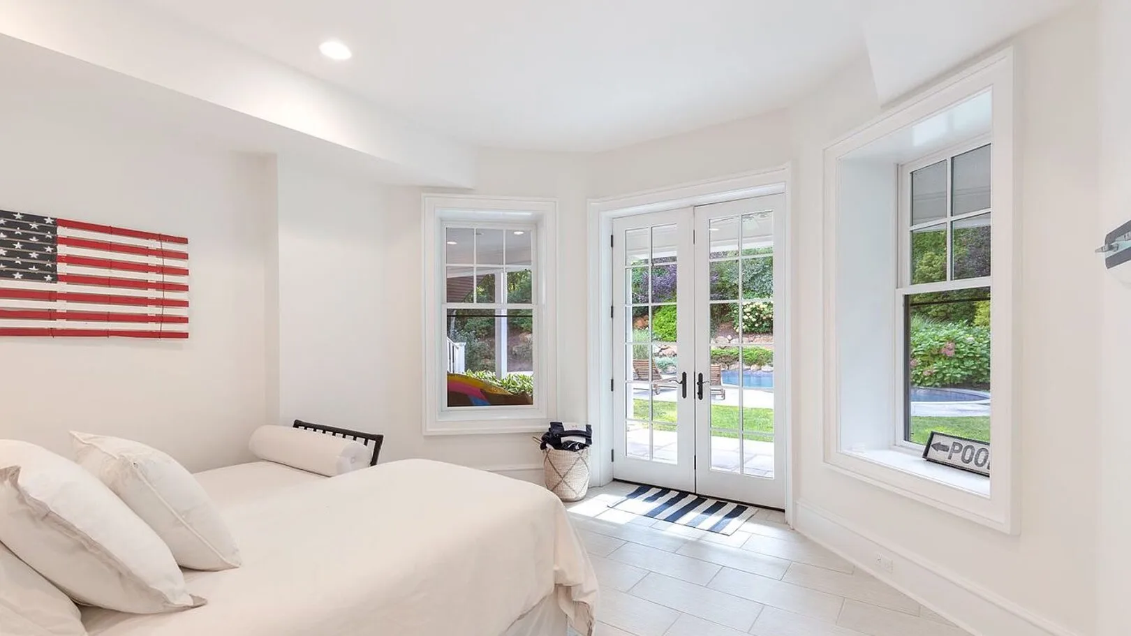 A bright bedroom with a bed beside windows and glass doors.