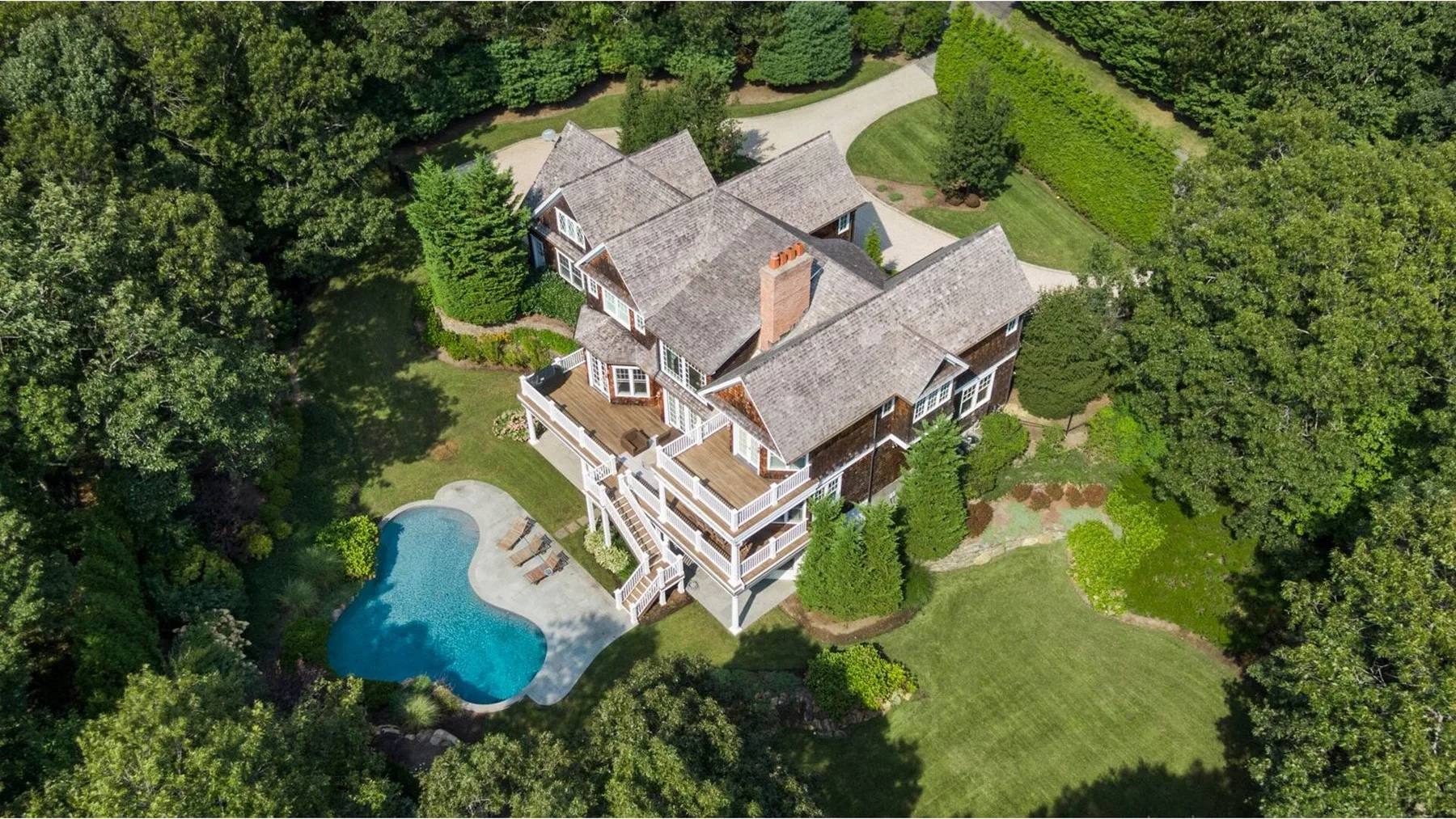 An aerial view of a large house surrounded by trees, with a swimming pool nearby.