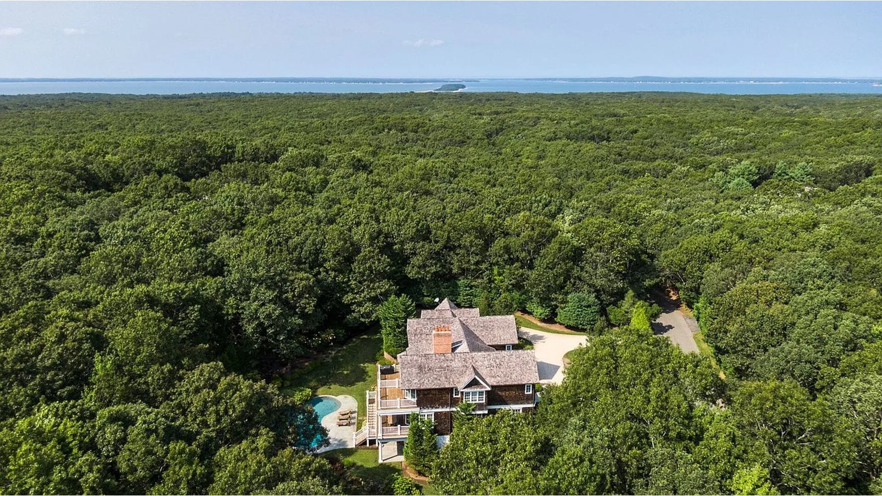 Aerial view of a house surrounded by dense forest, with the sea in the distance.