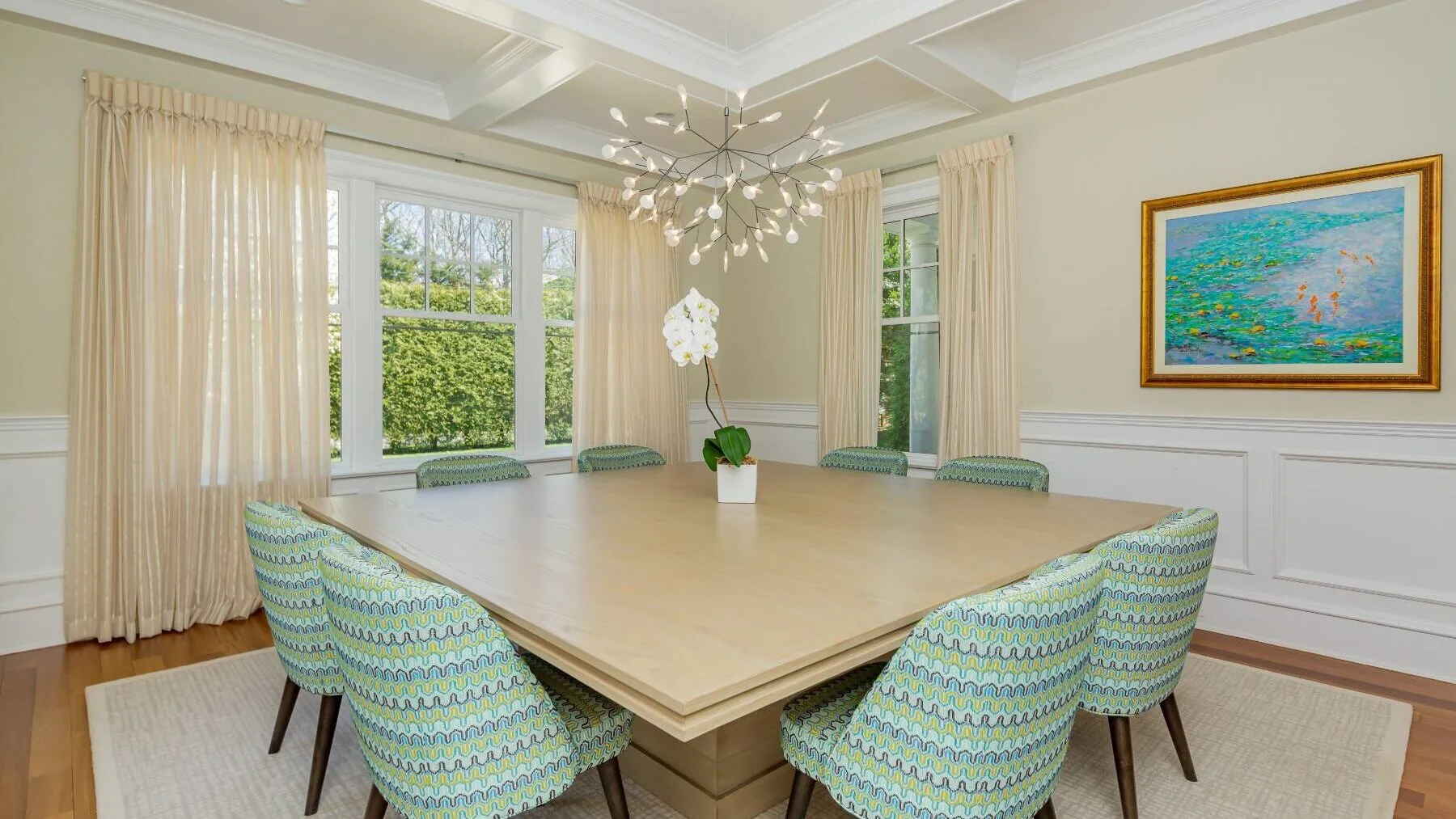 A dining room with a large table and upholstered seating beneath a chandelier.