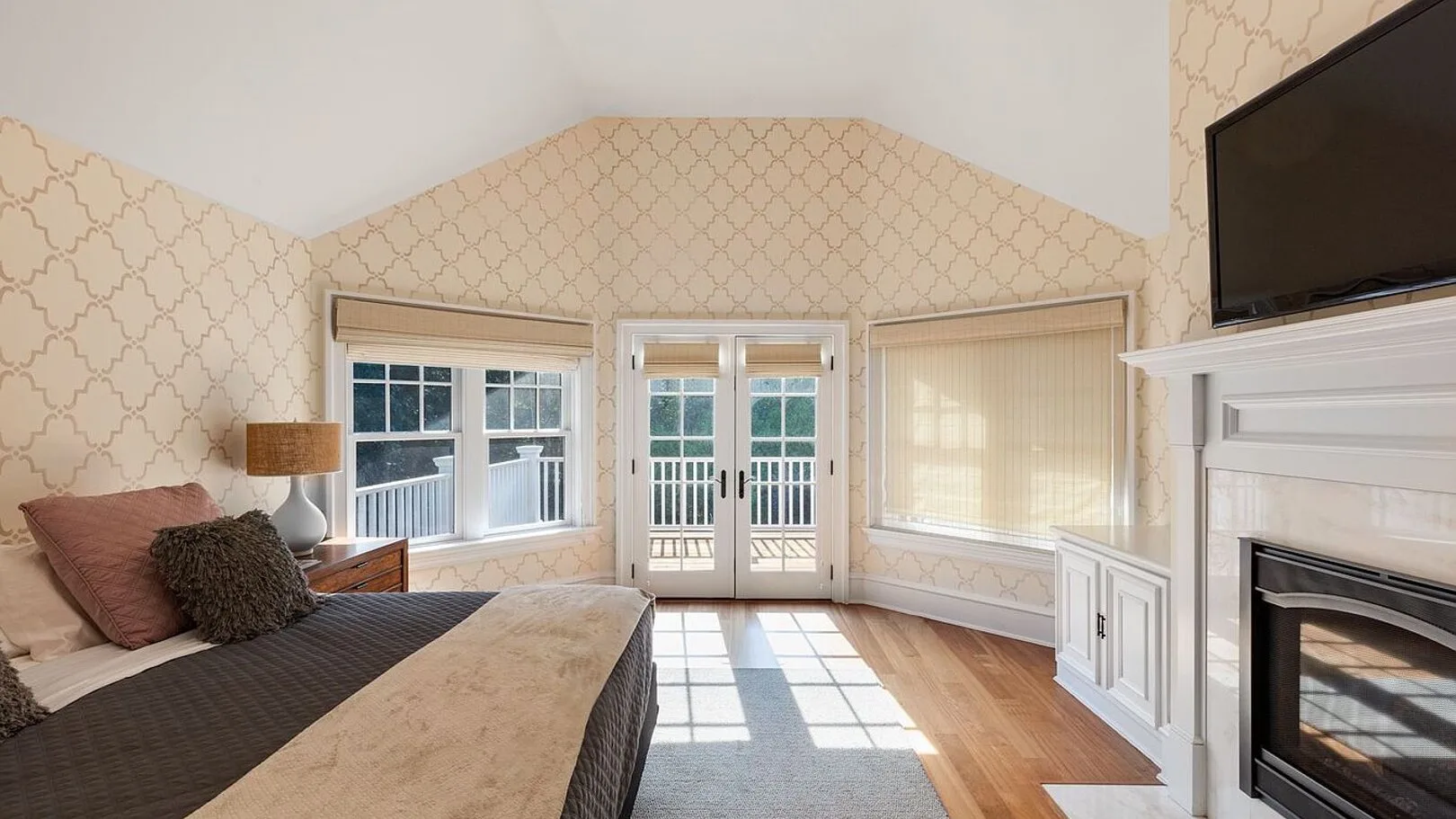 A bright bedroom with a bed, large windows, and a fireplace.