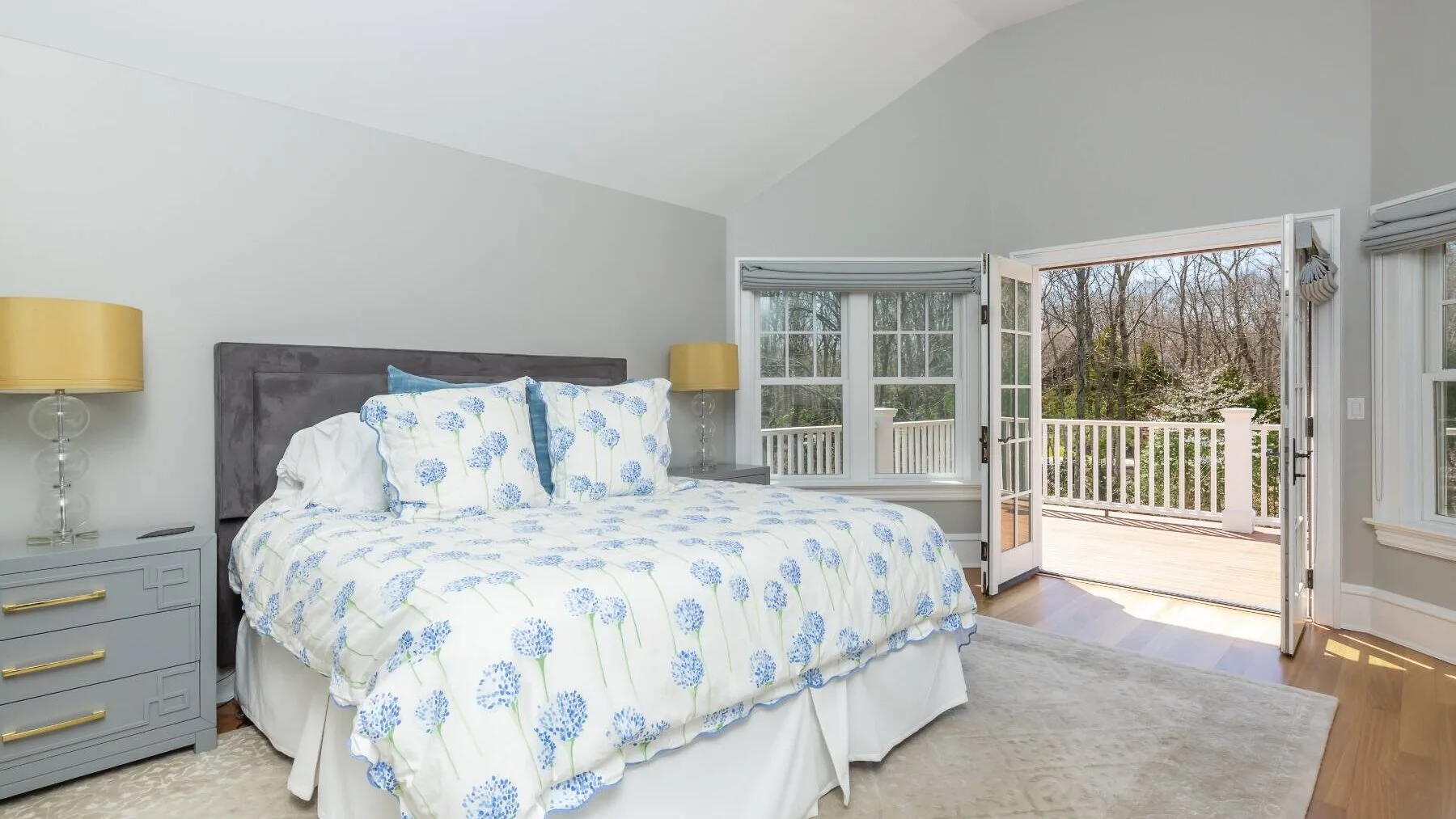 A bedroom with a bed dressed in blue floral bedding and open doors to a balcony.